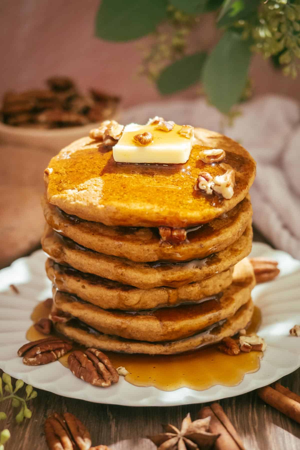 A stack of sweet potato pancakes with pecans, butter, and drizzle of maple syrup.